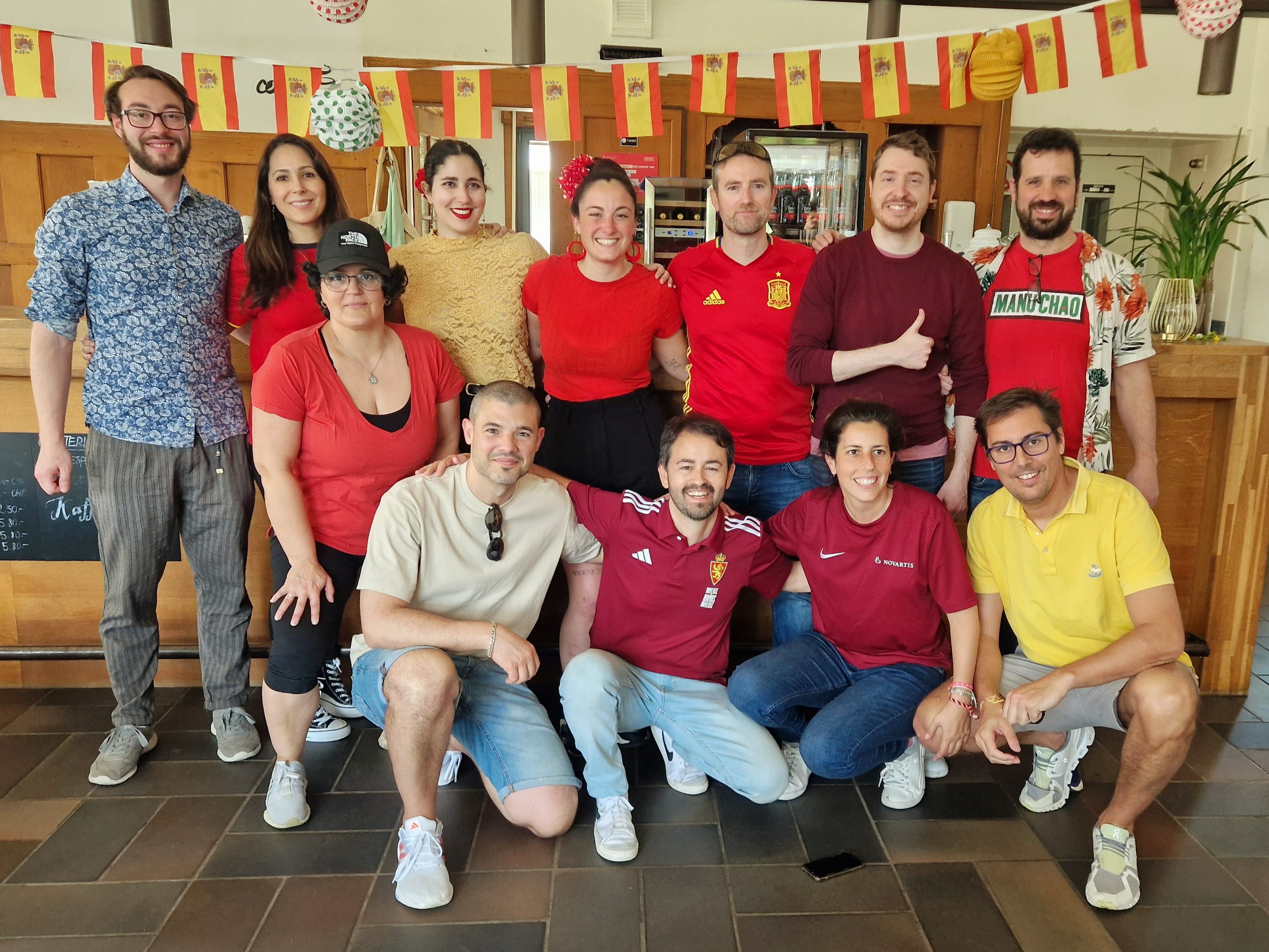 Group of volunteers posing together in a community space, smiling and wearing casual clothing, with decorations in the background celebrating Spanish culture.