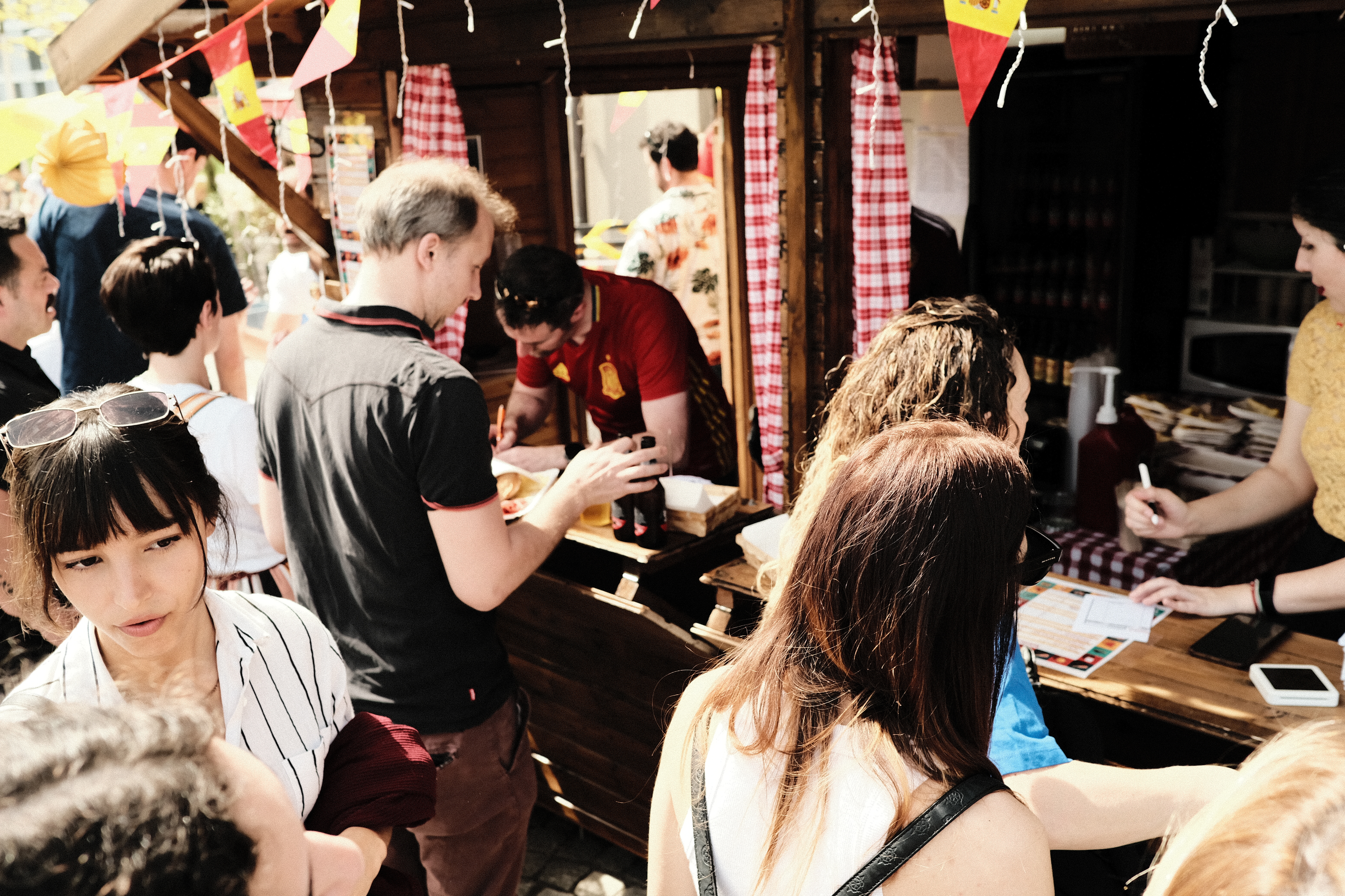 A crowded outdoor food stall at the Fiesta Española event, with people engaging with vendors and enjoying Spanish food and culture.